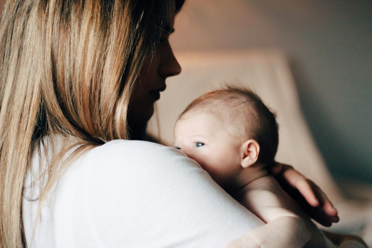 Elternteil hält ein Baby geborgen an der Schulter.